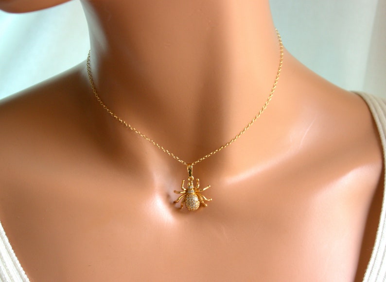 May include: A gold chain necklace with a sparkling spider pendant. The spider is made of gold and has clear stones for eyes.