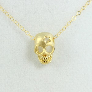 May include: A gold chain necklace with a gold skull pendant. The skull has a star cut out of the top of its head.
