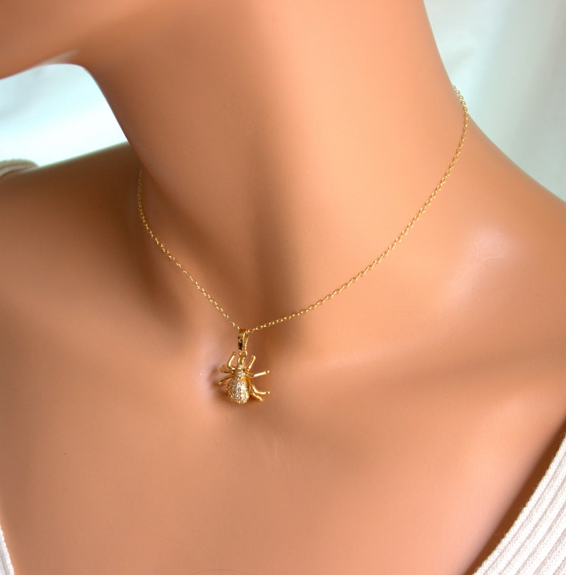 May include: A gold chain necklace with a small, sparkling spider pendant. The spider is made of gold and has clear crystals for its body and legs.
