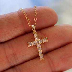 May include: A gold chain necklace with a small, sparkling cross pendant. The cross is adorned with clear cubic zirconia stones.