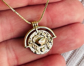 May include: Gold chain necklace with a round pendant featuring a detailed design of a crab. The pendant is attached to the chain with a small ring.