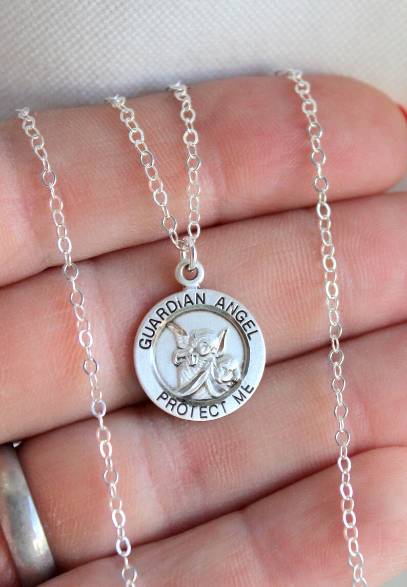 May include: Silver chain necklace with a round pendant featuring a guardian angel with the words "Guardian Angel Protect Me" around the edge.