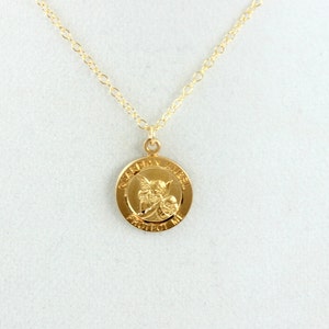 May include: Gold necklace with a round pendant featuring a guardian angel with the words "Guardian Angel Protect Me" inscribed around the edge.