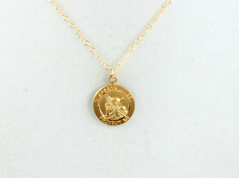 May include: Gold necklace with a round pendant featuring a guardian angel with the words "Guardian Angel Protect Me" inscribed around the edge.