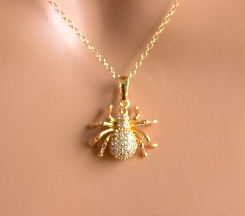 May include: A gold chain necklace with a sparkling spider pendant. The spider is made of gold and has clear rhinestones for eyes and body.