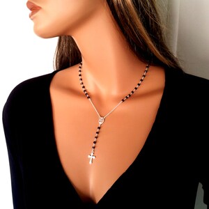 May include: A silver chain necklace with a small silver cross pendant and black beads. The necklace is worn by a person with long brown hair.