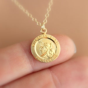 May include: Gold necklace with a round pendant featuring a guardian angel with wings and the words "Guardian Angel Protect Me".