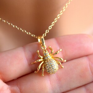 May include: A gold chain necklace with a sparkling spider pendant. The spider is made of gold and has clear rhinestones for eyes and body.