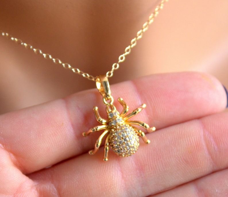 May include: A gold chain necklace with a sparkling spider pendant. The spider is made of gold and has clear rhinestones for eyes and body.