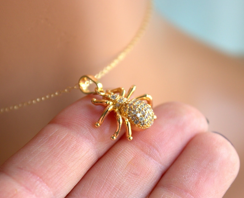May include: A gold necklace with a sparkling spider pendant. The spider is covered in clear rhinestones.