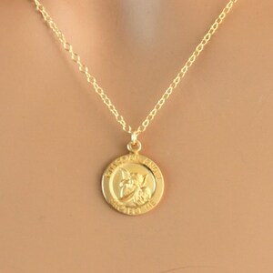 May include: Gold chain necklace with a round pendant featuring a guardian angel design and the words "Guardian Angel Protect Me".