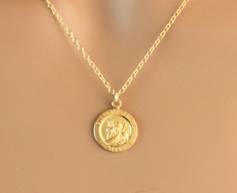 May include: Gold chain necklace with a round pendant featuring a guardian angel design and the words "Guardian Angel Protect Me".
