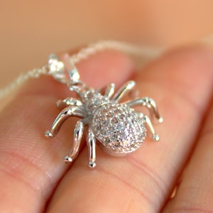 May include: A silver spider pendant necklace with clear cubic zirconia stones. The spider is detailed with eight legs and a round body.