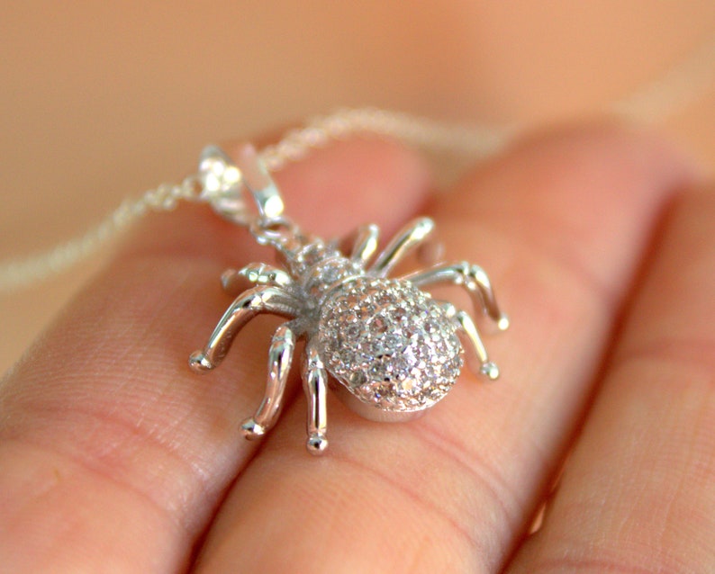 May include: A silver spider pendant necklace with clear cubic zirconia stones. The spider is detailed with eight legs and a round body.