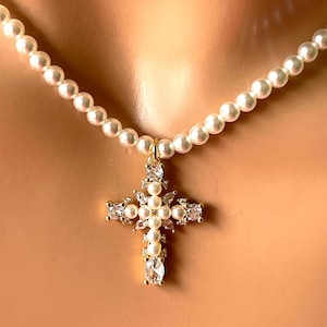 May include: A pearl necklace with a gold cross pendant. The cross is adorned with pearls and clear crystals. The necklace is composed of small, round, white pearls.