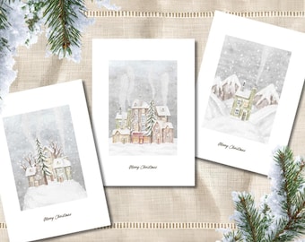 May include: Three white greeting cards featuring watercolour illustrations of snowy winter village scenes with houses, trees, and mountains. Each card displays the text Merry Christmas in a simple black script font at the bottom centre.