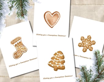 May include: Four white greeting cards featuring watercolour gingerbread illustrations of a heart, a stocking, a Christmas tree, and a snowflake. Each card displays the brown text, Wishing you a Scrumptious Christmas! The cards are arranged on a surface.