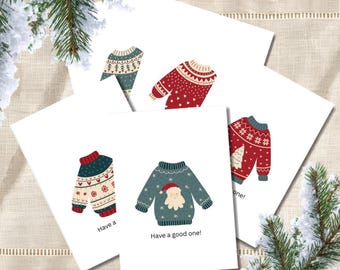 May include: A set of white greeting cards featuring illustrations of colourful holiday jumpers with patterns including trees, snowflakes, and a Santa face. One card displays the text Have a good one! and another shows the partial text Have a.