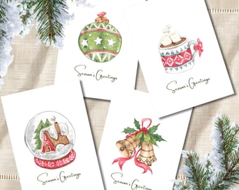 May include: Four white greeting cards featuring watercolour illustrations of a green Christmas ornament, a mug of hot cocoa with marshmallows, a snow globe with a house, and two gold bells with holly, each with the text Season's Greetings.
