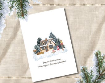 May include: A white Christmas greeting card featuring a watercolour illustration of a snow-covered cottage, pine trees, a snowman, and a sled. The text reads: From our Home To Yours Wishing you a Wonderful Christmas!