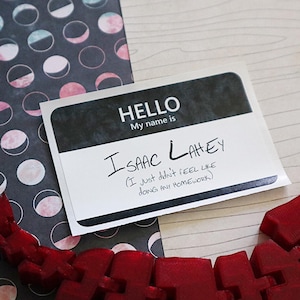 May include: A white name tag with black text that reads "HELLO My name is ISAAC LAHEY (I just didn't FEEL LIKE DOING ANY HOMEWORK)"