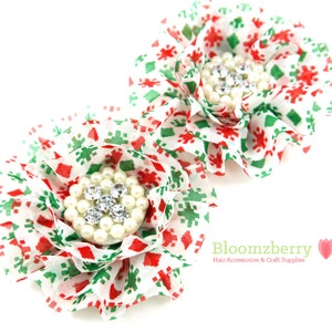 May include: Two red and green snowflake patterned fabric flowers with white pearl and rhinestone embellishments.