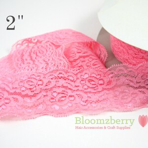 May include: Pink lace ribbon, 2 inches wide, with a floral pattern. The ribbon is partially unrolled from a white spool. The Bloomzberry logo is visible in the bottom right corner.