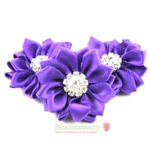 May include: Three purple satin flower hair clips with rhinestone centers.