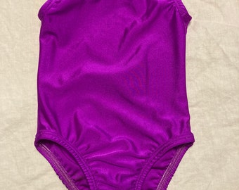 May include: A purple sleeveless leotard with a scoop neck. The leotard is made of a shiny, stretchy fabric.