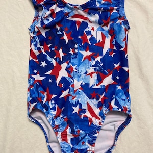 May include: A white, blue, and red leotard with a stars and stripes pattern. The leotard has a scoop neck and sleeveless design.
