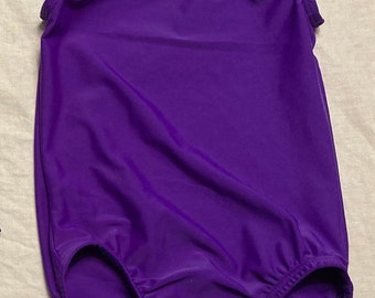 Puede incluir: Un leotardo morado sin mangas con cuello redondo y un fondo fruncido.