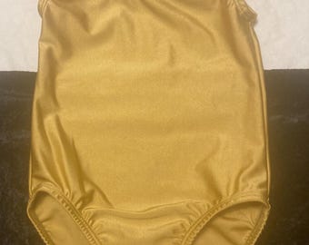 May include: A sleeveless leotard in a solid metallic gold color. The garment features a scoop neckline and a high-cut leg design with finished seams along the armholes and leg openings, crafted from a smooth, shiny, and stretchy fabric.