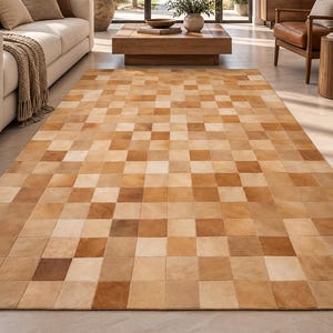 May include: A rectangular area rug featuring a patchwork design composed of square tiles in varying shades of tan, beige, cream, and light brown. The rug displays a consistent grid pattern across its entire surface, showcasing natural color variations.
