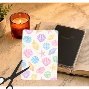 May include: A rectangular protective case for an e-reader featuring a repeating pattern of pastel-colored seashells and starfish in shades of pink, blue, yellow, purple, and green against a white background, shown with a clear plastic shell.