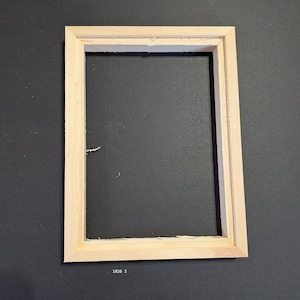 May include: A rectangular, light-colored wooden picture frame with a simple, flat profile and mitered corners. The frame is empty, showing a hollow center. The text 1026 3 is printed in small white font at the bottom center of the frame.