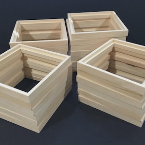 May include: A collection of four square wooden frames arranged in two stacks. Each frame is constructed from light-colored, unfinished wood with a visible grain, featuring a hollow center and a simple, clean-lined, open-box structure.