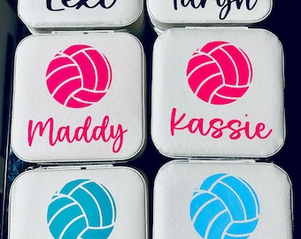 May include: Six white square jewelry boxes with a volleyball graphic and a name on each. The names are Lexi, Taryn, Maddy, Kassie, Kennedie, and Hayden. The volleyballs are in different colors: black, pink, blue, and teal.