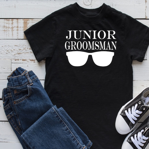 May include: Black t-shirt with white text that reads "Junior Groomsman" and a pair of sunglasses.