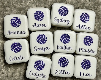 May include: Twelve white square jewelry boxes with a volleyball graphic and a name on each box. The names are:  Arianna, Ava, Sydney, Allie, Sonja, Kaitlyn, Maddie, Celeste, Calysta, Ella, Lia.