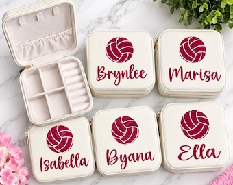 Puede incluir: Cinco joyeros de viaje cuadrados de color crema con cremalleras doradas. Cuatro joyeros están cerrados, cada uno con un gráfico de voleibol rosa oscuro y un nombre personalizado: Brynlee, Marisa, Isabella, Byana o Ella. Uno está abierto.