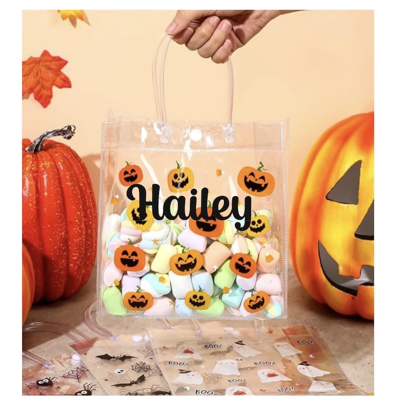May include: Clear plastic Halloween-themed gift bag filled with colorful marshmallows. The bag is decorated with jack-o'-lantern stickers and the name "Hailey" in black script. Two orange pumpkins are in the background.