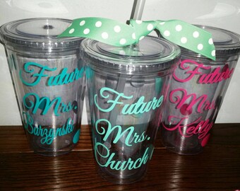 May include: Three clear plastic cups with lids and straws. Each cup has a different name written on it in teal, pink, and turquoise lettering. The cups say "Future Mrs. Barzynski", "Future Mrs. Church", and "Future Mrs. Kelly".