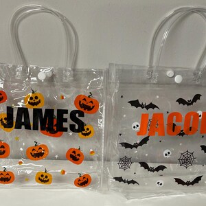 May include: Clear plastic Halloween treat bags with clear handles. One bag has orange pumpkins and the name "JAMES" in black. The other bag has black bats, spiderwebs, skulls, and the name "JACOB" in orange.