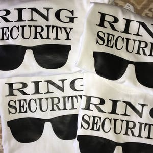 May include: Four white t-shirts with black text and sunglasses graphics. The text on the shirts reads "Ring Security".