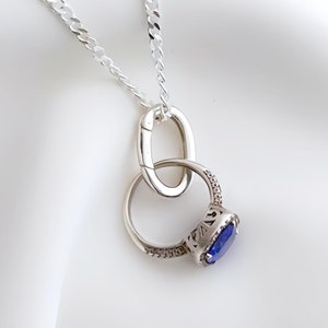 Könnte beinhalten: Eine silberne Kettenkette mit einem silbernen Ringanhänger. Der Ring hat einen blauen Edelstein und ist mit kleineren Steinen besetzt.