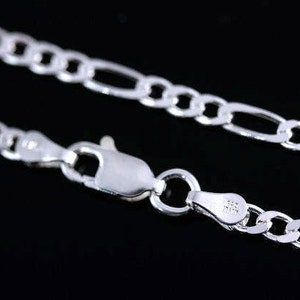 May include: A silver Figaro chain necklace featuring a polished finish and a lobster claw clasp. The metal tag near the clasp is stamped with the text 925 and ITALY, indicating the material composition and origin of the jewelry piece.