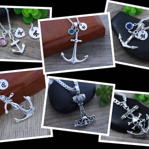 May include: A collection of silver-toned metal necklaces featuring anchor and hammer pendants. Some designs include circular charms engraved with letters like K, M, or P, and small round colored crystals. One pendant features a skull and crossbones.