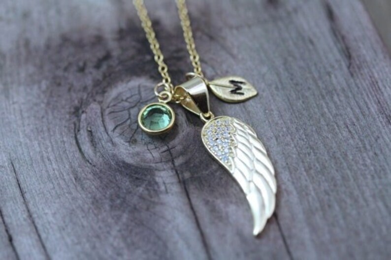 May include: Gold necklace with a green gemstone, a small leaf charm with the letter "M" and a silver wing charm with clear rhinestones.