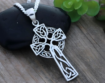 May include: A silver-toned Celtic cross pendant featuring intricate knotwork patterns throughout the cross and the circular halo. The pendant is attached to a silver-toned chain, showcasing a polished metallic finish with detailed engravings.