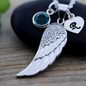 May include: Silver angel wing pendant necklace with a turquoise blue gemstone and a silver heart charm with the letter R.